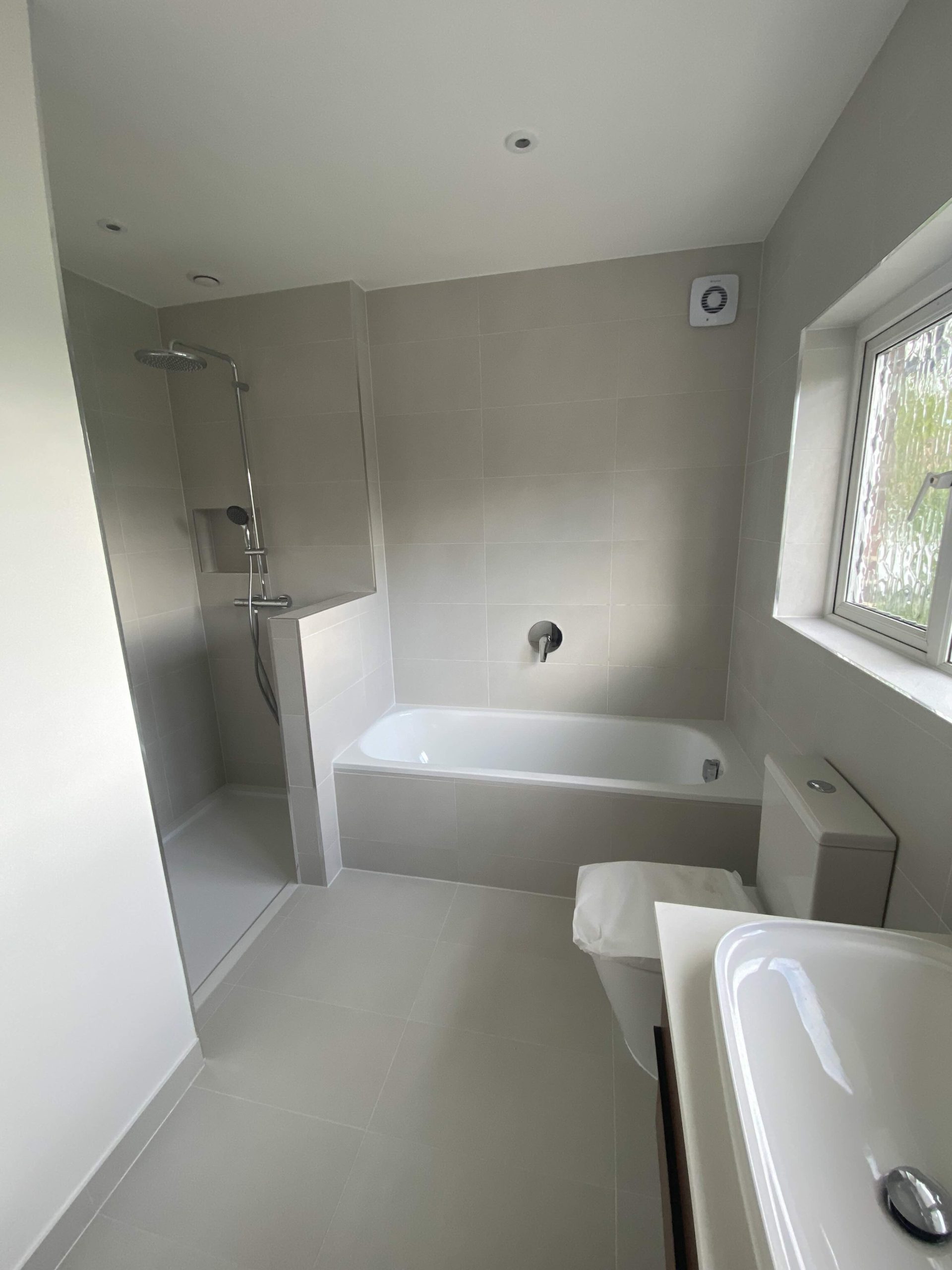 Completed modern bathroom with walk-in shower, bath, recessed shower niche, and mechanical ventilation installed.