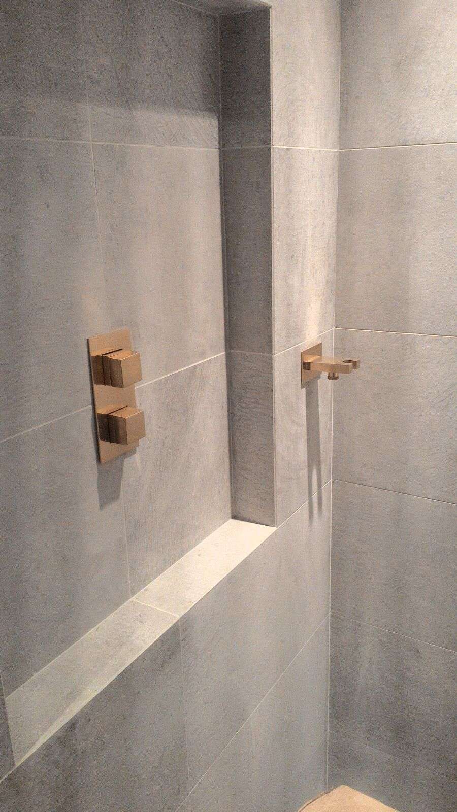Walk-in shower with large-format porcelain tiles, recessed shower niche, and concealed brushed brass shower controls.