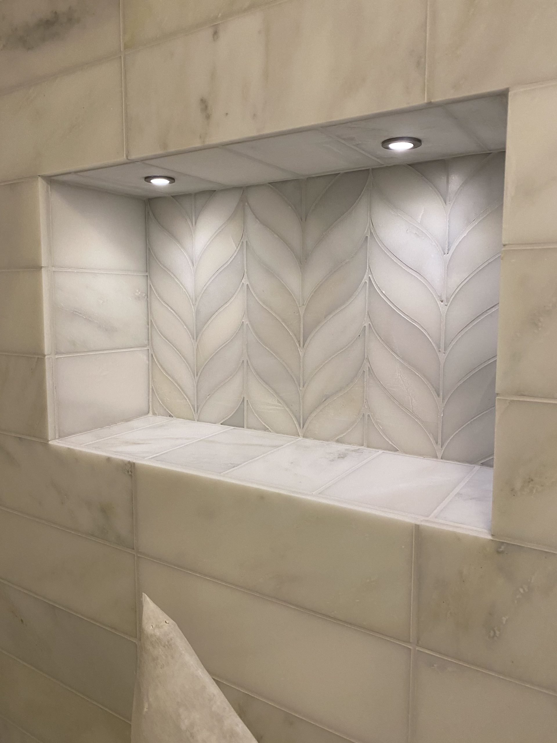Illuminated recessed shower niche with decorative feature tiles and integrated LED spotlights.